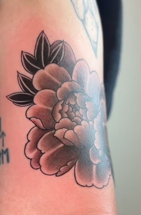 Soft black-and-grey peony with dark leaves on an upper arm