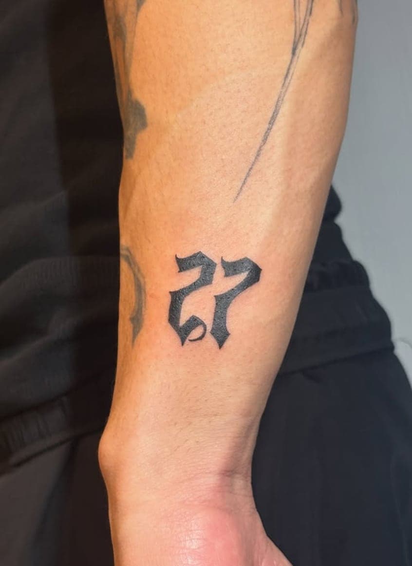 Brushy blackletter numerals 27 on the side of a forearm
