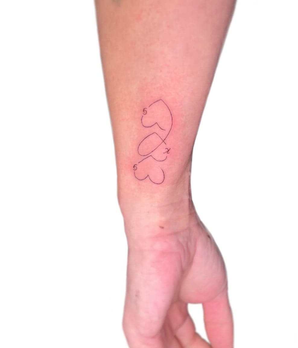 Three hearts drawn in a single unbroken fine line with initials, on a wrist