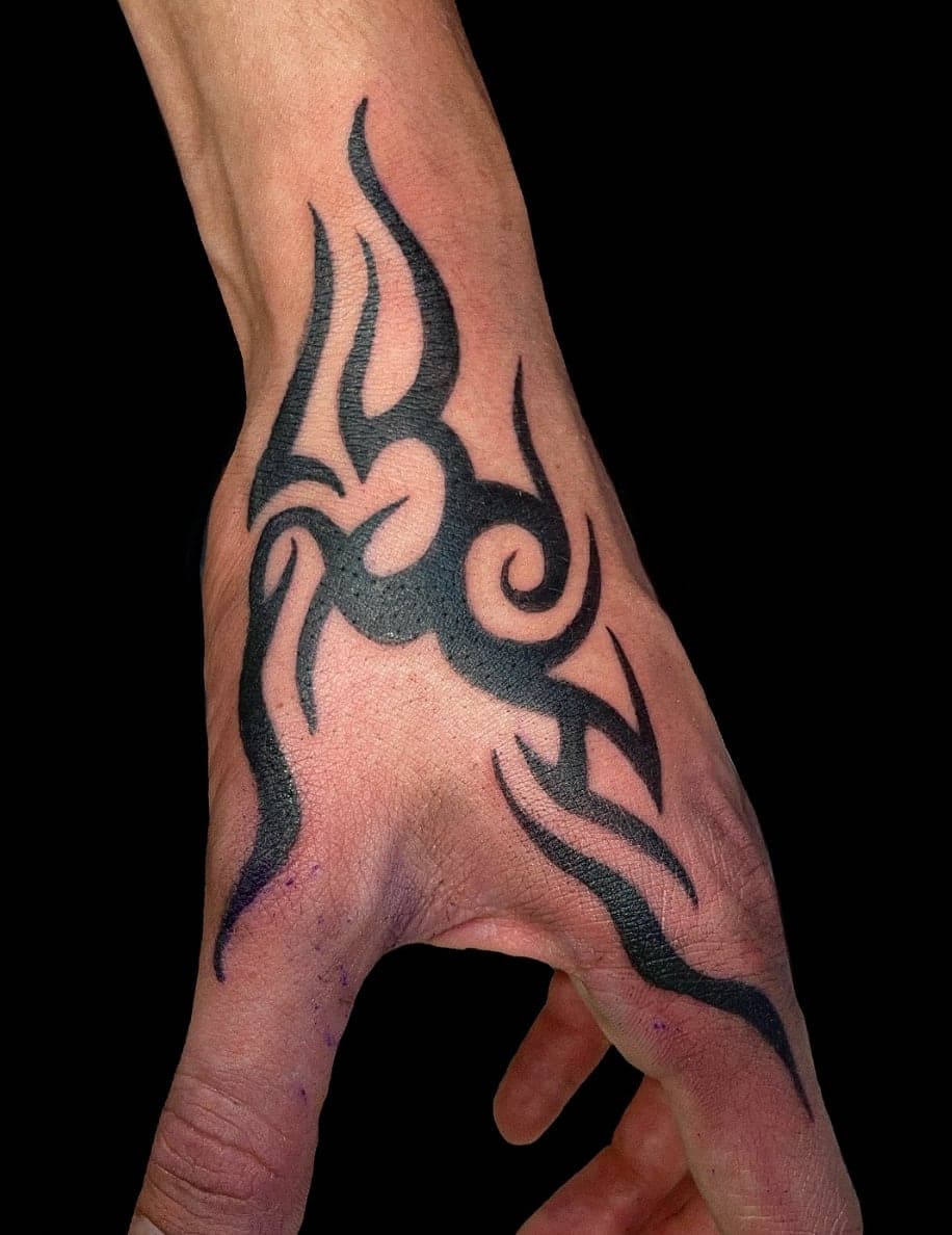 Bold tribal blackwork flowing across the back of a hand